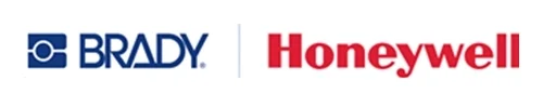 Vue d'ensemble d'un espace de travail moderne et lumineux de collaboration entre Honeywell et Brady, baptisé « Honeywell Brady Collaborative Asset Identification Solution ». Au premier plan, des employés testent des scanners de codes-barres et des imprimantes d'étiquettes posés sur une table. En arrière-plan, une banderole verticale affiche les logos « Honeywell » et « Brady » avec le slogan « Partners for end-to-end visibility », ainsi que de grands portraits muraux et un écran de présentation montrant un schéma de workflow.